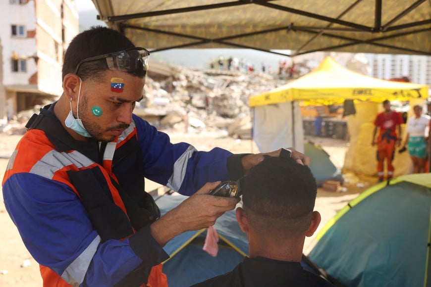 A Venezuelan volunteer rescuer with a Venezuelan flag painted on his forehead cuts the hair of a fellow volunteer at a temporary camp set up to assist in the aftermath of the June 24 earthquakes, in La Guaira, Venezuela, July 16, 2026. REUTERS/Leonardo Fernandez Viloria