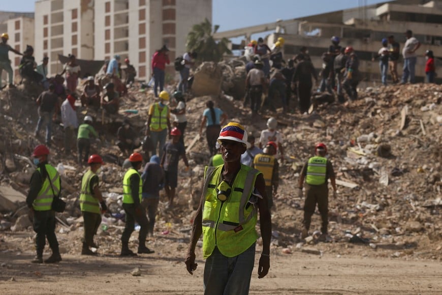 A search and rescue volunteer wearing a Venezuelan flag attached to his helmet searches debris alongside other people, in the aftermath of the June 24 earthquakes, in La Guaira, Venezuela, July 16, 2026. REUTERS/Leonardo Fernandez Viloria