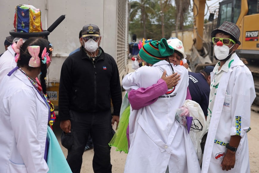 Members of the Venezuelan NGO "Doctor Yaso, Payasos de Hospital," dressed in clown costumes, comfort a volunteer rescuer as people search for their loved ones beneath the rubble in the aftermath of the June 24 earthquakes in La Guaira, Venezuela, July 18, 2026. REUTERS/Leonardo Fernandez Viloria