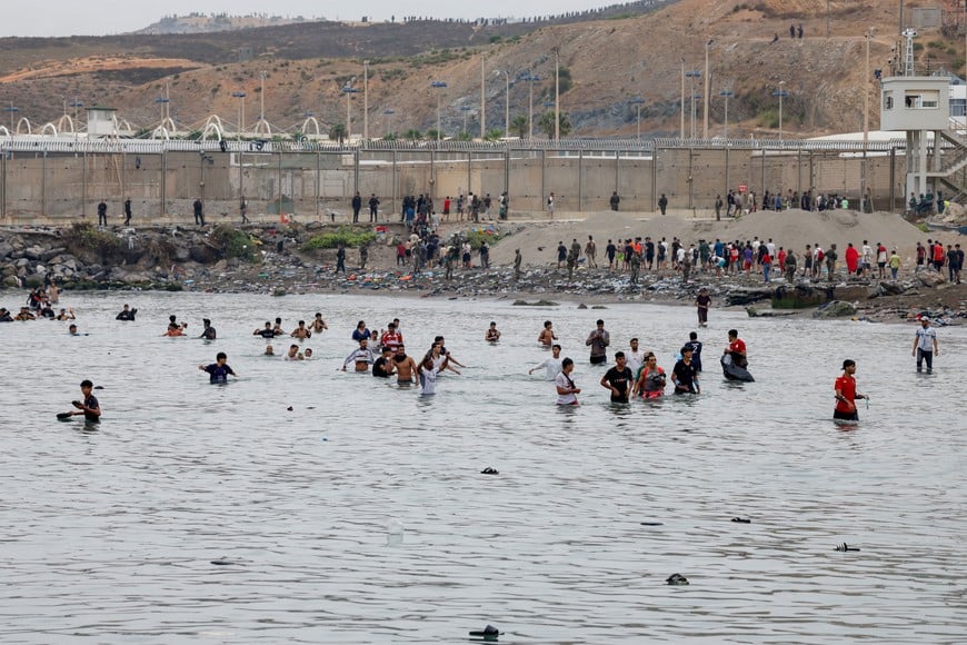 People waddle through water to enter Spain, and in the background people who just entered Spain return back to Morocco, amid mass crossings of migrants on foot and by sea from Morocco into Spanish territory, in Ceuta, Spain, July 31, 2026. REUTERS/Jon Nazca
REFILE - CHANGES SLUG