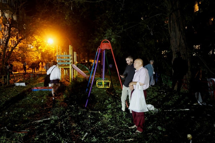 People stand together as a man looks on at the site of an apartment building hit by a Russian missile strike, amid Russia's attack on Ukraine, in Kyiv, Ukraine, August 1, 2026. REUTERS/Gleb Garanich