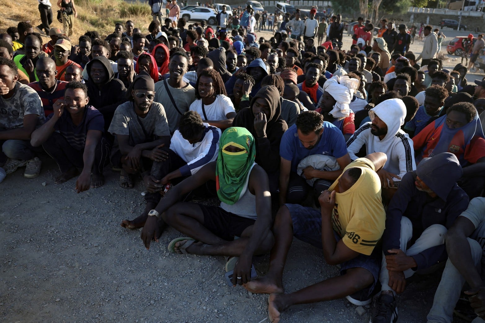 Migrantes hacen fila para recibir alimentos y bebidas de la Cruz Roja, tras los cruces masivos de migrantes a pie y por mar desde Marruecos.