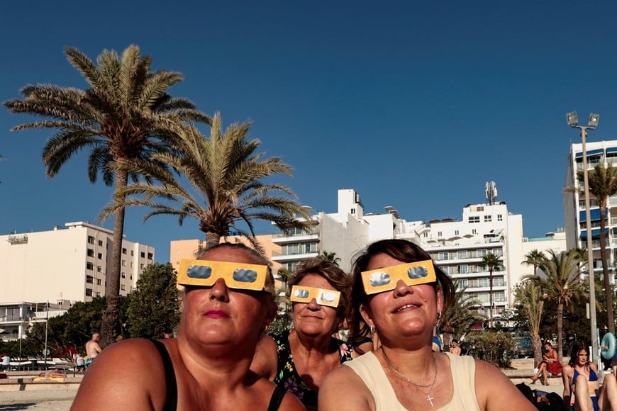 People from Cologne, Germany, test their protective glasses ahead of a solar eclipse, at El Arenal beach in Mallorca, Spain, August 12, 2026. REUTERS/Francisco Ubilla