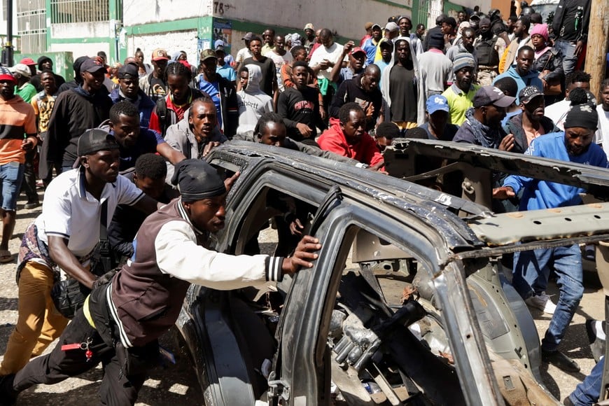 Residents push the wreckage of a car during a protest against insecurity after a fatal overnight raid by an armed gang, on the outskirts of Port-au-Prince, in Kenscoff, Haiti, August 24, 2026. REUTERS/Fildor Pq Egeder