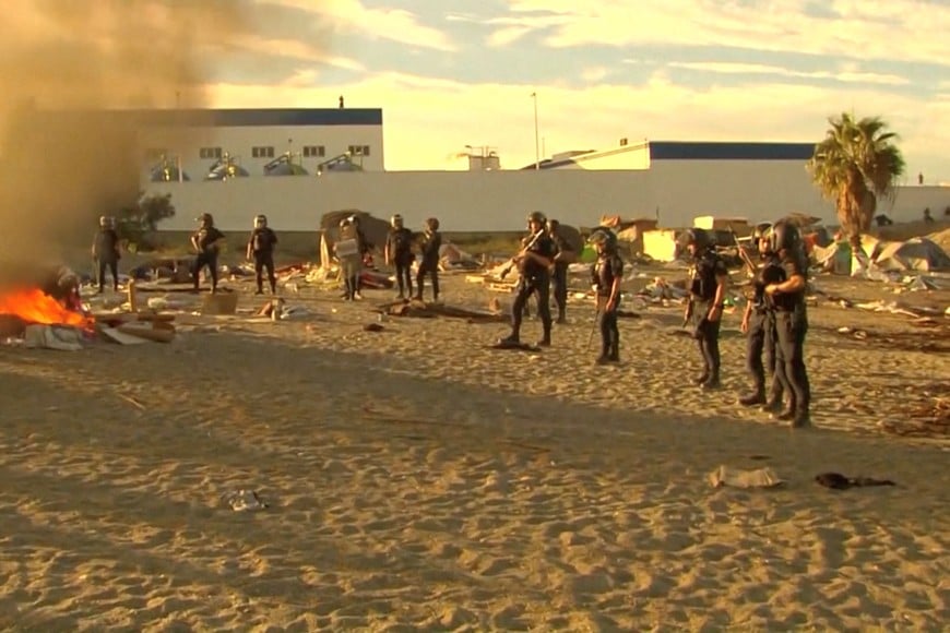 Law enforcement personnel stand while smoke and flames rise as Ceuta residents destroy migrant camp by the beach, in Ceuta, Spain, August 27, 2026, in this screen grab taken from a handout video. FORTA/Handout via REUTERS THIS IMAGE HAS BEEN SUPPLIED BY A THIRD PARTY. SPAIN OUT. NO COMMERCIAL OR EDITORIAL SALES IN SPAIN
