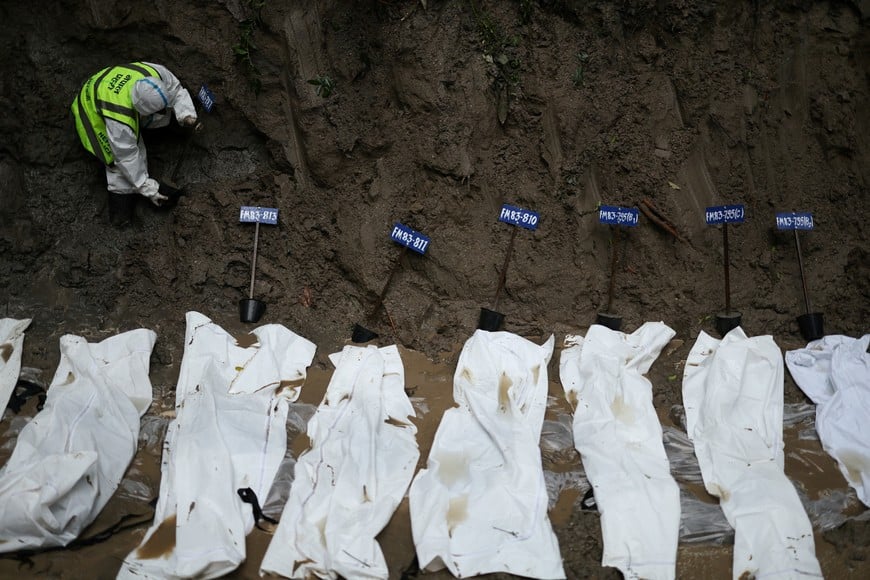 A security personnel member handles a victim identification tag, next to bodies lined up in the pit at a mass burial site for victims of deadly flash floods and mudslides, in Gokarna forest, Kathmandu, Nepal, September 1, 2026. REUTERS/Athit Perawongmetha