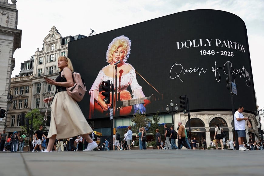 People walk past a tribute to U.S. country singer Dolly Parton at Piccadilly Circus, a day after the announcement of her death at age 80, in London, Britain, August 26, 2026. REUTERS/Hiba Kola