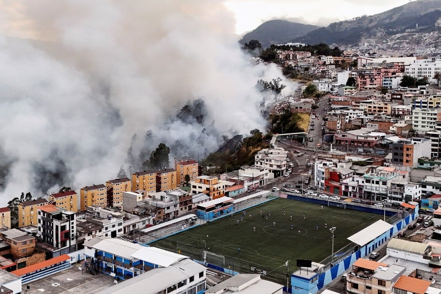 A drone view shows smoke rising from a hillside during a wildfire near residential neighbourhoods while people play soccer on a field in Quito, Ecuador, September 13, 2026. REUTERS/Karen Toro TPX IMAGES OF THE DAY