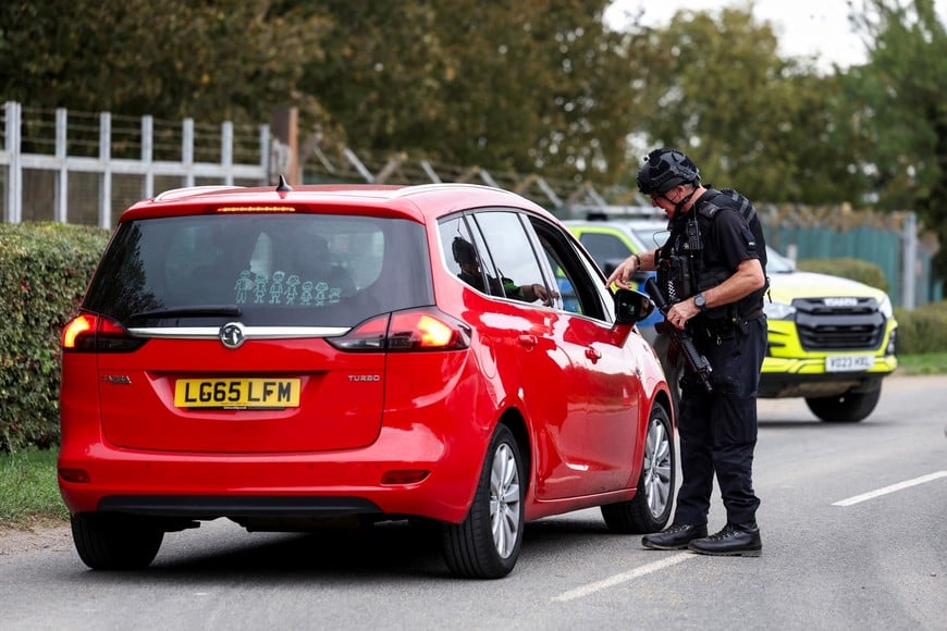 A police officer speaks to the driver of a vehicle on a road outside the perimiter of the RAF Fairford airbase, after police declared a major incident at the base after several men were arrested on suspicion of offences under the Explosives Act, in Fairford, Gloucestershire, Britain, September 27, 2026. REUTERS/Toby Shepheard