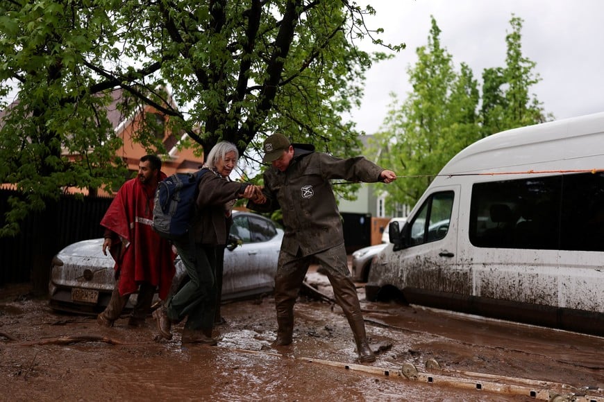 A police officer (carabinero) helps a person cross a mud-filled street after heavy rains triggered a mudslide in Santiago, Chile, October 8, 2026. REUTERS/Pablo Sanhueza