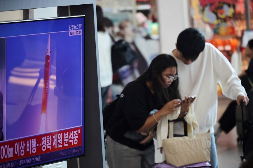 A couple looks at a mobile phone next to a TV broadcasting a news report on North Korea firing multiple ballistic missiles toward the sea off its east coast, at a railway station in Seoul, South Korea, October 12, 2026. REUTERS/Kim Hong-Ji