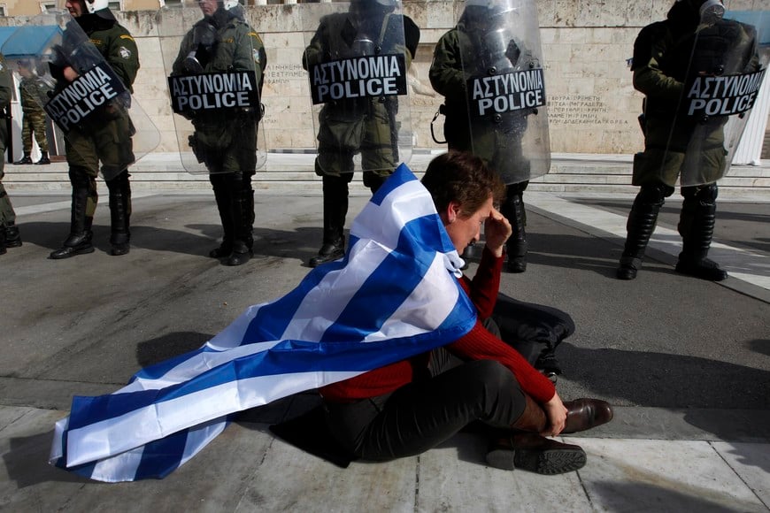 An anti-austerity protester draped with a Greek flag sits in front of police guarding parliament in Athens February 11, 2012 during a demonstration on the second day of a 48-hour strike by Greek workers unions. The Greek government told rebellious lawmakers on Saturday to back a deeply unpopular EU/IMF rescue in parliament or send the nation down "an unknown, dangerous path" to default and international economic isolation. REUTERS/Yannis Behrakis (GREECE - Tags: BUSINESS POLITICS CIVIL UNREST) grecia atenas grecia crisis economica ajuste plan austeridad del gobierno paro huelga general protestas manifestaciones