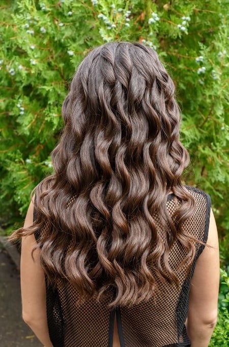Back view of brunette woman with long dark curly hair on garden background. Long glossy curly hair. Curly hair. Hairstyle back view