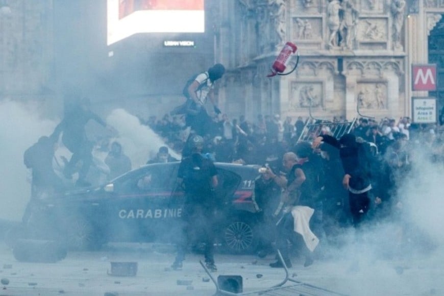 Manifestantes violentos atacan un patrullero de los Carabinieri durante graves disturbios en la Plaza del Duomo.