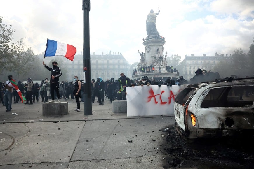 A masked protester holds a French flag next a burning car amid clashes with the French police during a demonstration at the Place de la Republique in Paris as part of nationwide protests against the cost of living and rising fuel prices called by the "Yellow Vests" movement, joined by French high school and university students, teachers and parents demanding better school conditions and government action, as well as labour unions, workers, farmers and retirees, France, October 17, 2026. REUTERS/Abdul Saboor