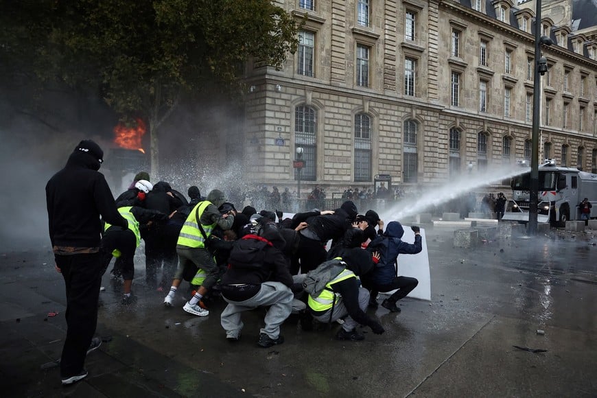 Protesters take cover behind a barricade as French riot police use water canon amid clashes during a demonstration at the Place de la Republique in Paris as part of nationwide protests against the cost of living and rising fuel prices called by the "Yellow Vests" movement, joined by French high school and university students, teachers and parents demanding better school conditions and government action, as well as labour unions, workers, farmers and retirees, France, October 17, 2026. REUTERS/Abdul Saboor