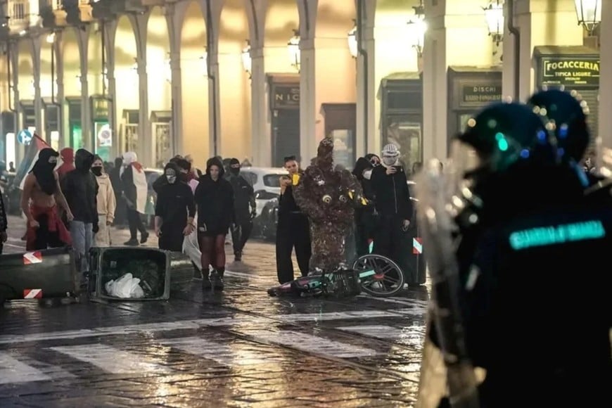 Una línea de la Guardia di Finanza italiana con equipo antidisturbios vigila a manifestantes encapuchados.