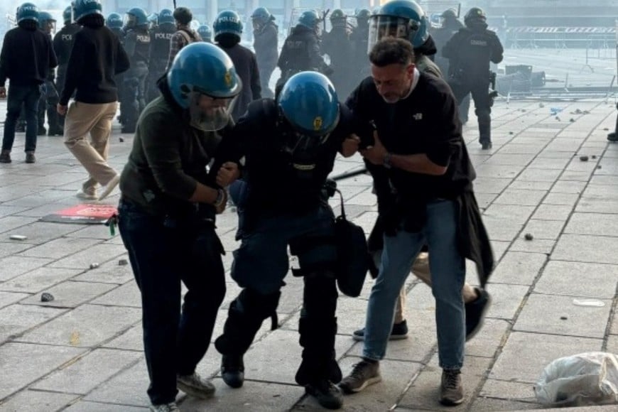 Un efectivo de la Policía italiana es asistido por sus compañeros tras resultar herido en los enfrentamientos registrados en la Plaza del Duomo en Milán.