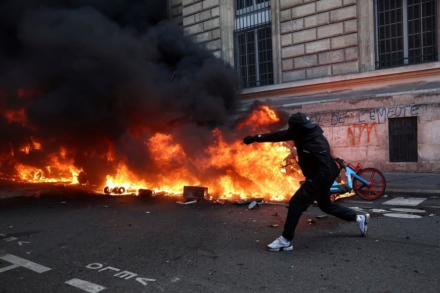 A masked protester throws an object onto a burning car amid clashes with the French police during a demonstration in Paris as part of nationwide protests against the cost of living and rising fuel prices called by the "Yellow Vests" movement, joined by French high school and university students, teachers and parents demanding better school conditions and government action, as well as labour unions, workers, farmers and retirees, France, October 17, 2026. REUTERS/Abdul Saboor