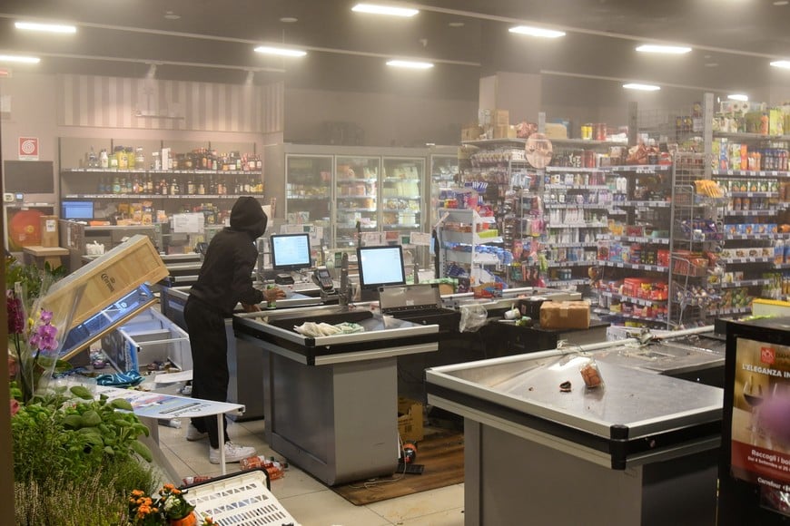 A hooded demonstrator stands near a checkout counter inside a damaged supermarket during a protest over the state of public services and the rising cost of living in Milan, Italy, October 18, 2026. REUTERS/Stringer
