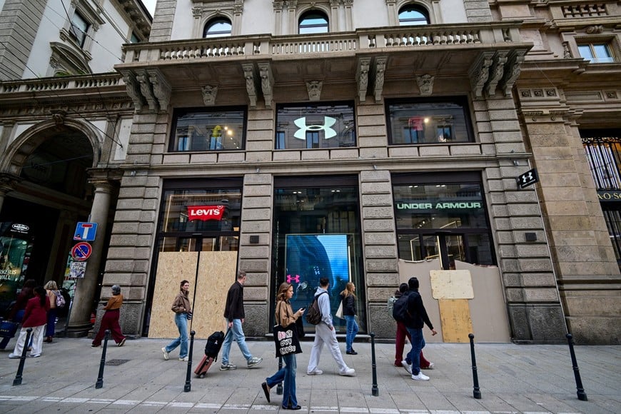Pedestrians walk past boarded-up Levi's and Under Armour storefronts following weekend clashes between police and protesters in Milan, Italy, October 19, 2026. REUTERS/Daniele Mascolo