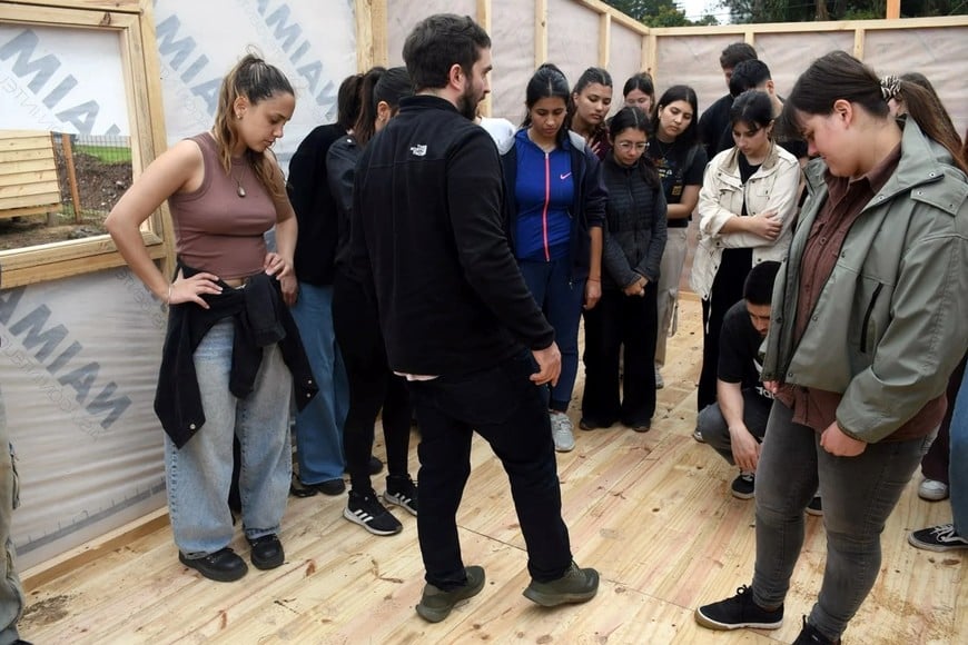 Estudiantes de la UNL y voluntarios observan las especificaciones técnicas del suelo de madera elevado durante la instrucción práctica.