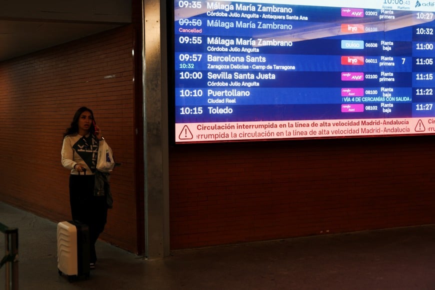 A woman with a suitcase walks past an information screen at the Atocha train station that says that the high-speed train line between Madrid and Andalucia has been interrupted, following the collision of two high-speed trains between the towns of Mora and Orgaz, in Madrid, Spain, October 28, 2026. REUTERS/Susana Vera