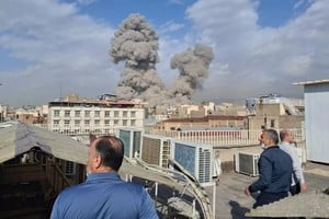 Iraníes observan cómo el humo se eleva hacia el horizonte después de una explosión en Teherán, 28 de febrero de 2026.