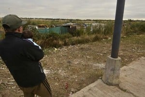 Un padre sostiene a su criatura junto a los ranchos levantados en la zona de bañados del oeste de la ciudad, junto a los reservorios. Fernando Nicola. Archivo.